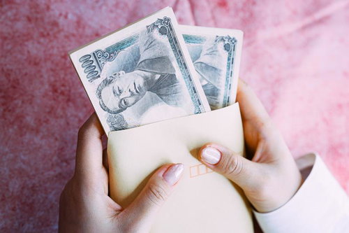 茶色い封筒から取り出した札束を持つ女性の手元