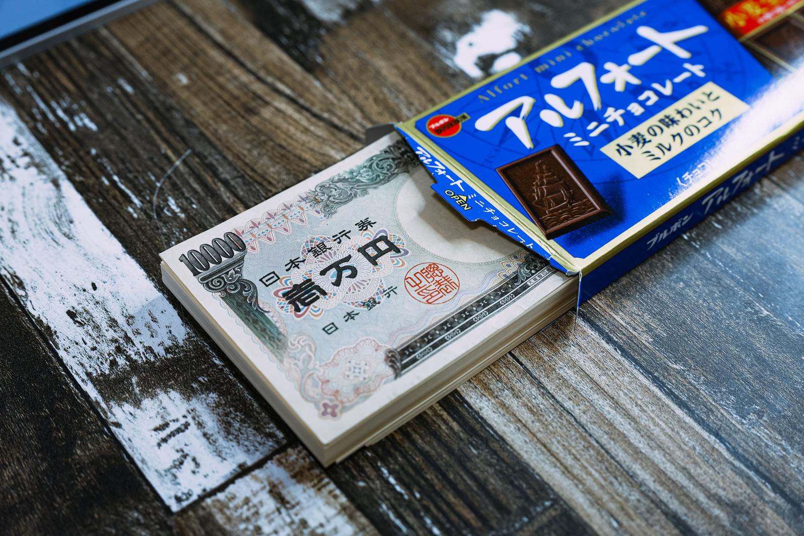一万円札と洋菓子パッケージが並ぶ貯金イメージ