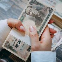 札束を握りしめる女性の手元、複数枚の一万円札を両手で握るの写真