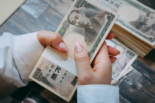 札束を握りしめる女性の手元、複数枚の一万円札を両手で握る