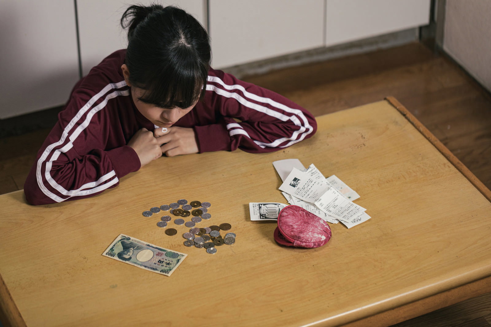 テーブルで小銭を数える赤いジャージの女学生［モデル：千歳］