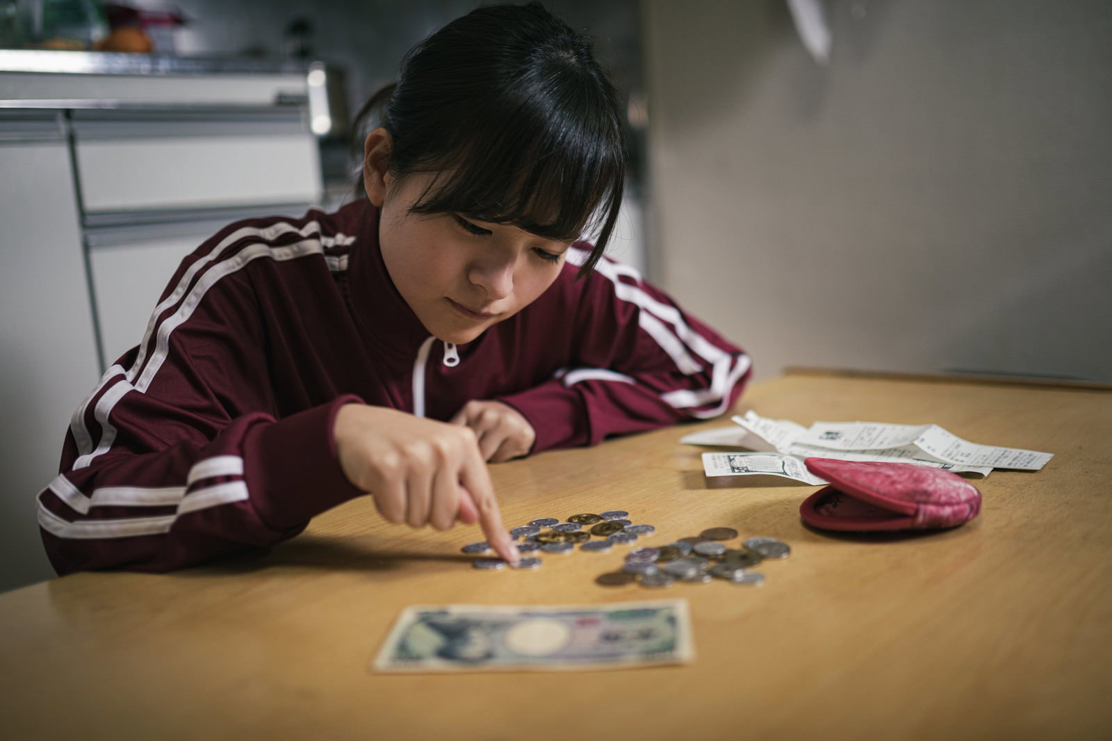 テーブルで小銭を数えながら生活費を切り詰める女子学生［モデル：千歳］