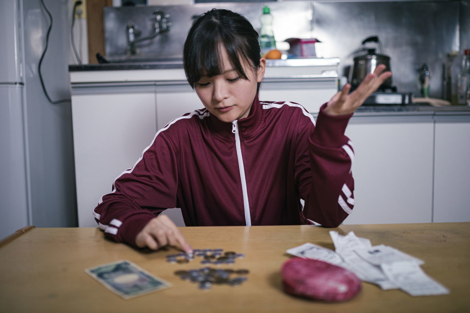 テーブルの上で小銭を数えながら困った表情をする女学生［モデル：千歳］