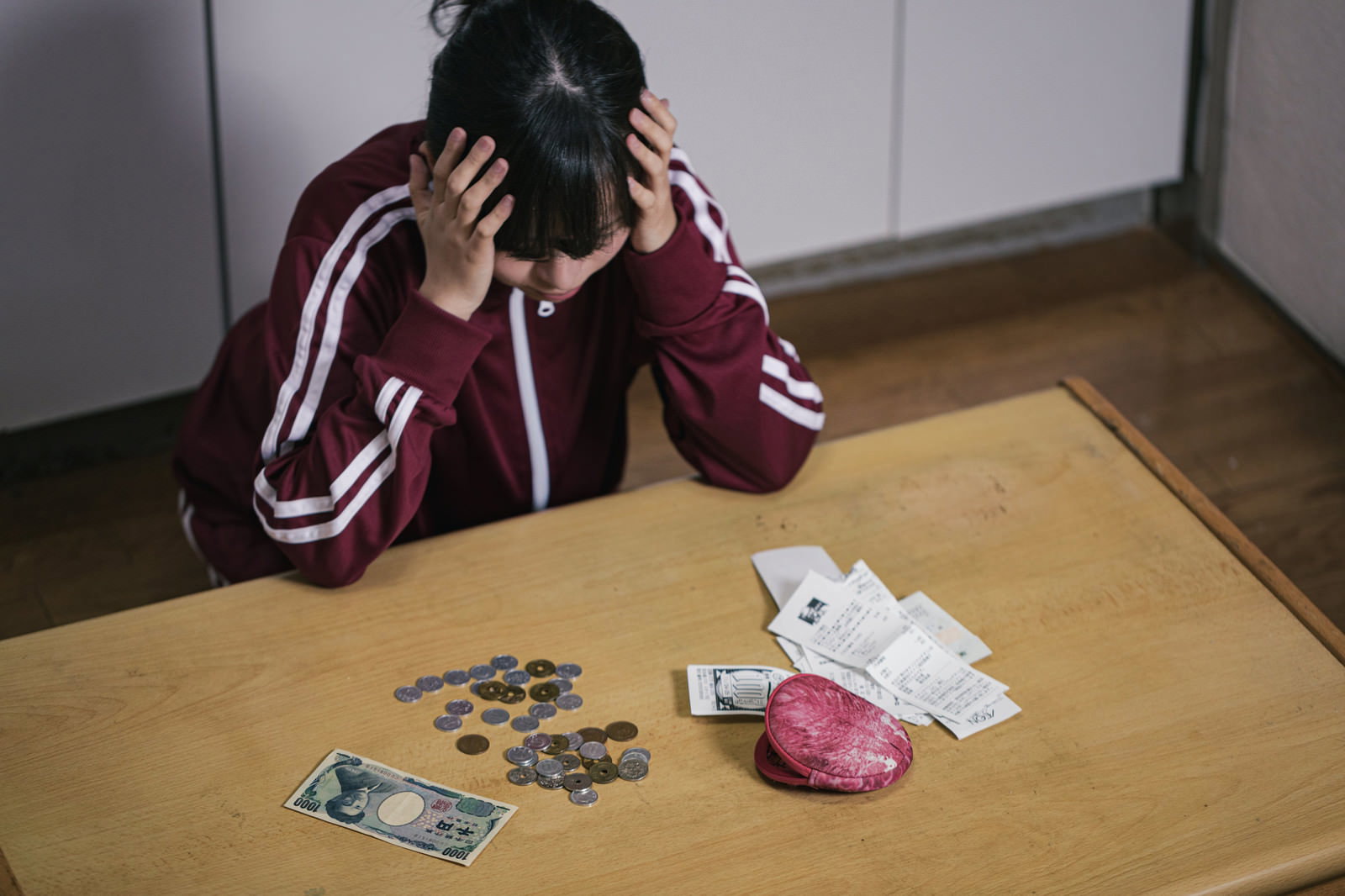 テーブルに小銭とレシートを置いて頭を抱えて悩む女性［モデル：千歳］
