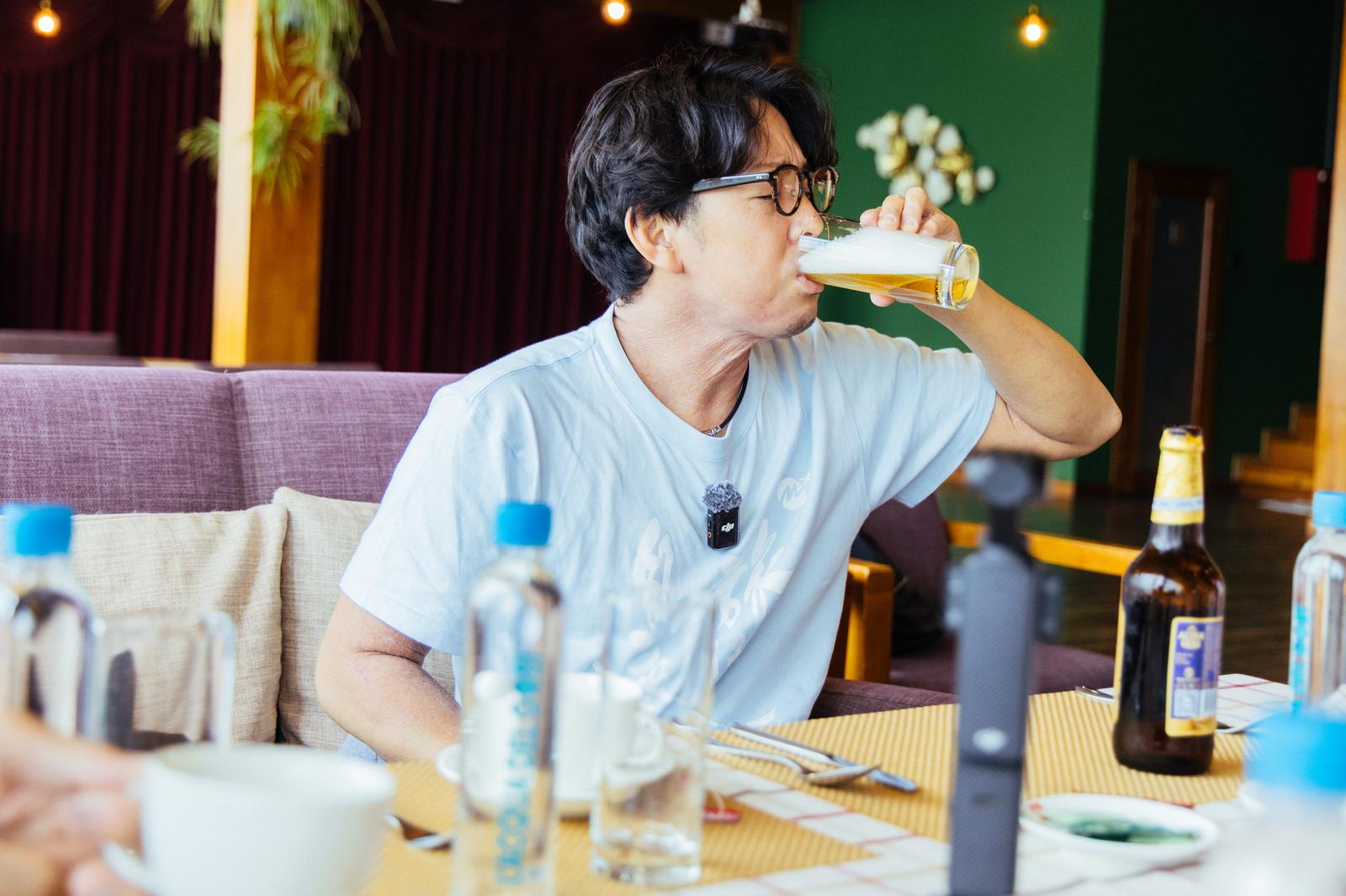 ビールを飲む眼鏡をかけた男性。テーブルに複数の飲料瓶［モデル：もーりー］