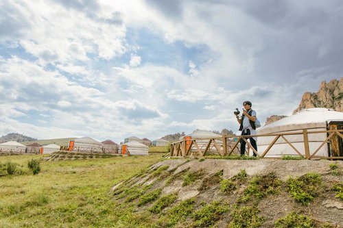 モンゴルの草原に広がるゲルの風景をカメラに収める男性旅人