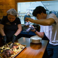 厨房で肉料理を撮影するYouTuberと調理する料理人の写真