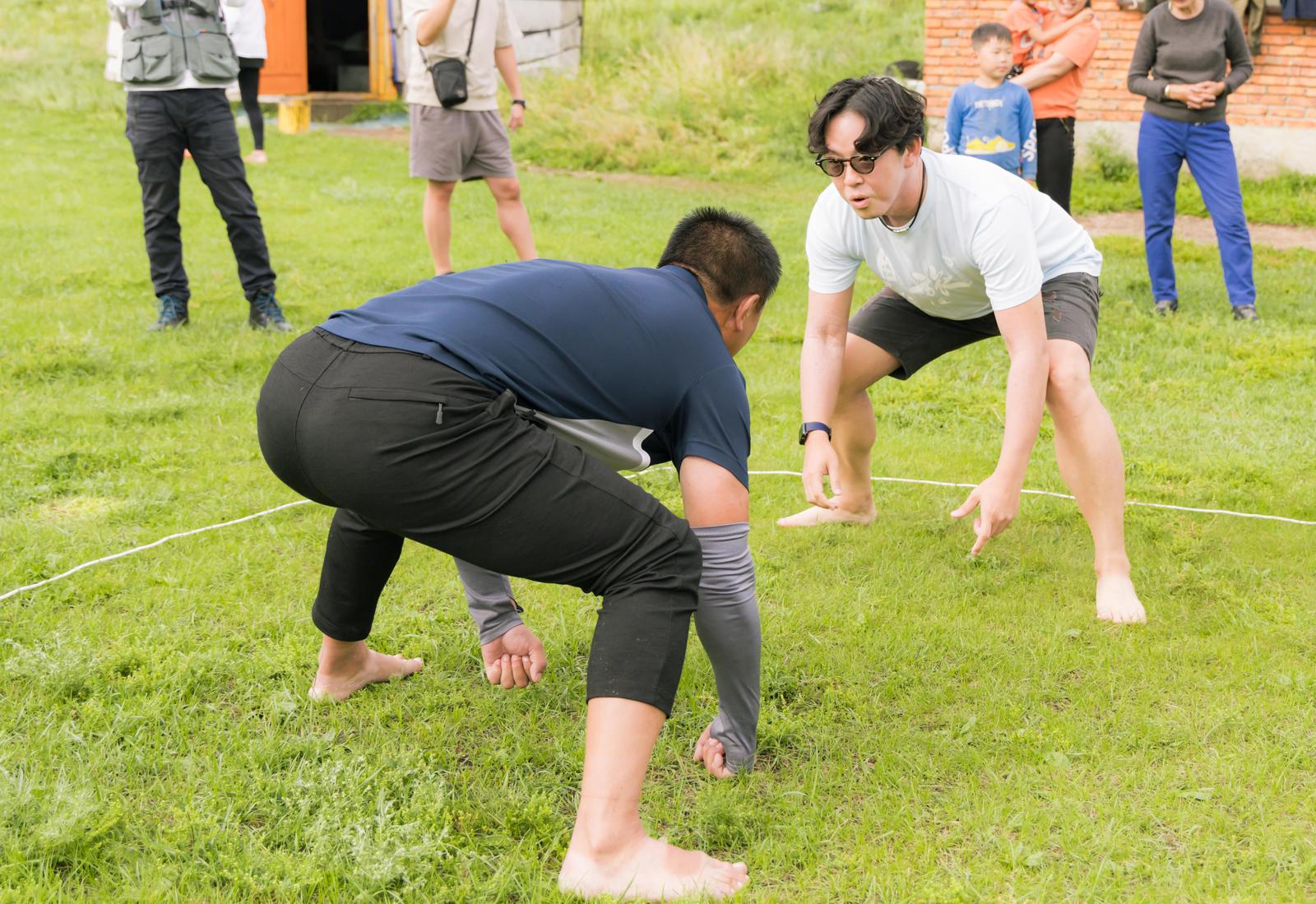 芝生の上で裸足で対戦するモンゴル相撲の力士と観衆［モデル：もーりー］