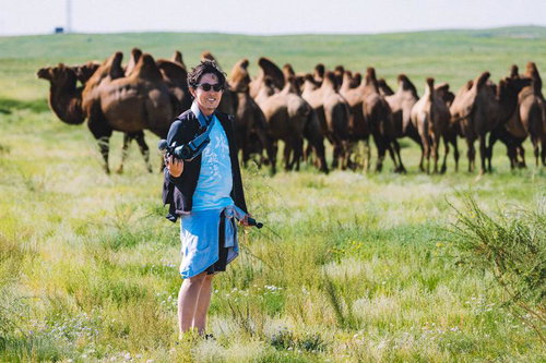 モンゴルの草原でラクダの群れを撮影するYouTuberの男性