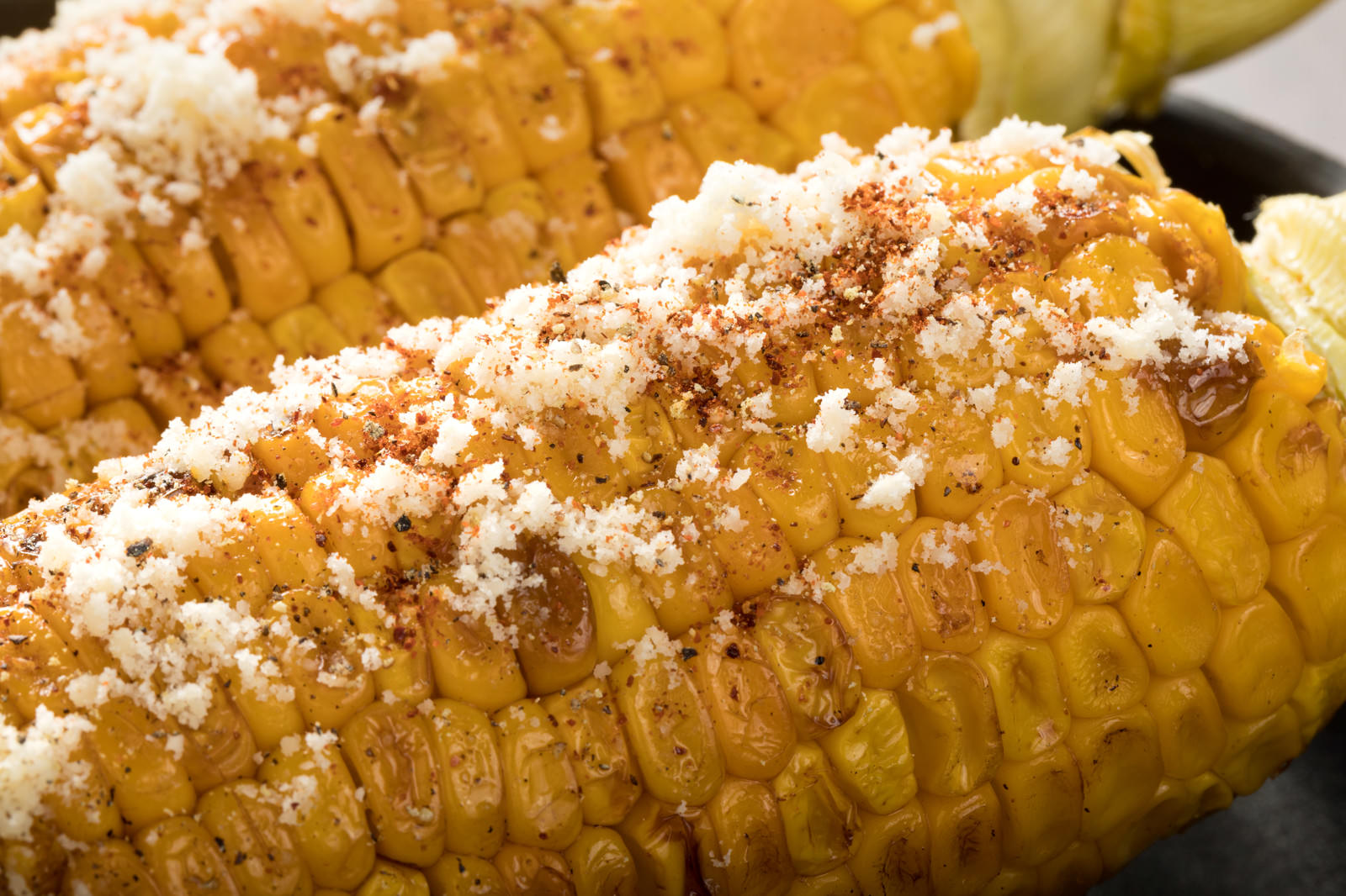 パルメザンチーズと黒胡椒がたっぷりかかった焼きとうもろこし