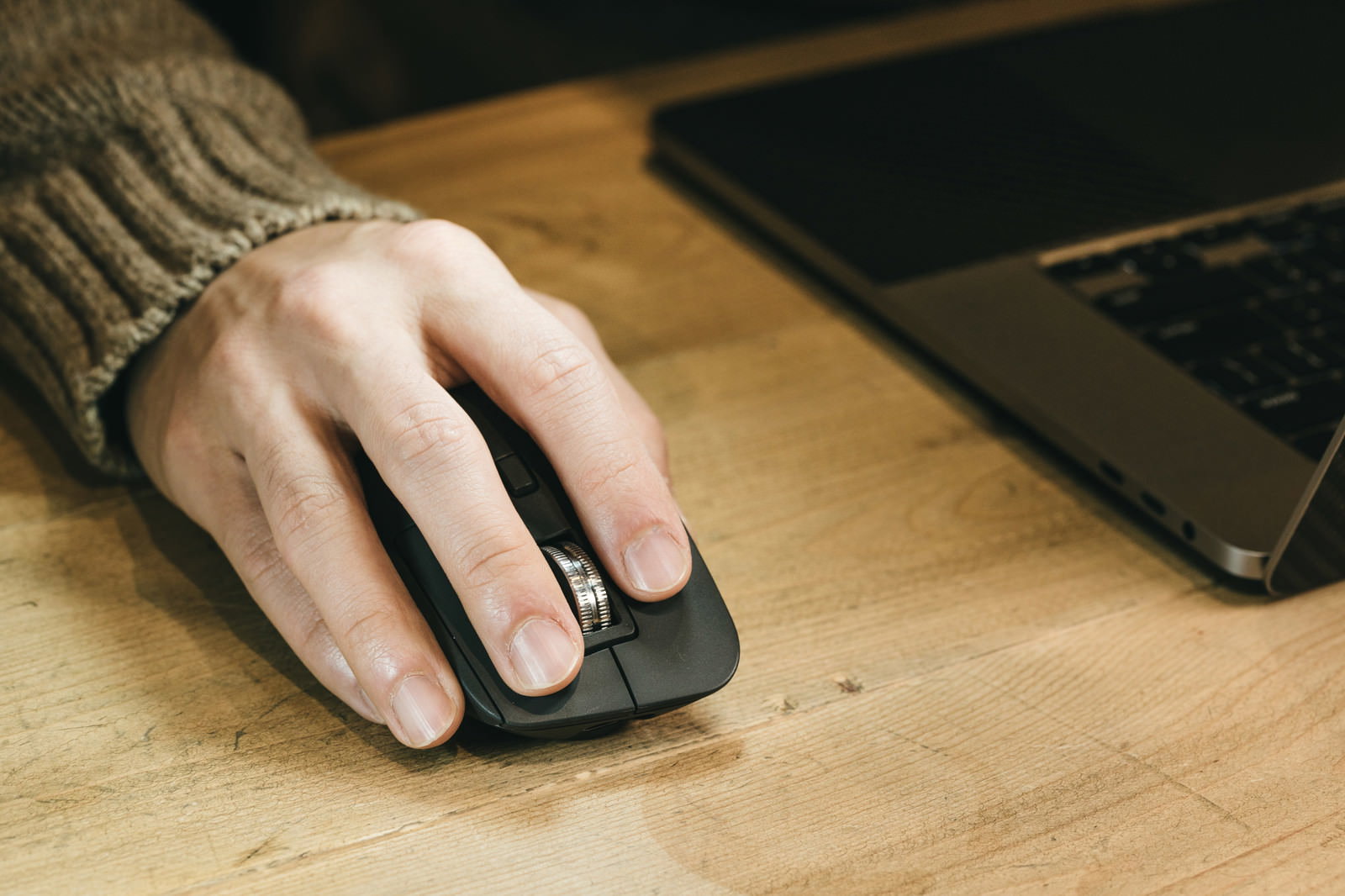 Right hand operating a mouse on a wooden desk