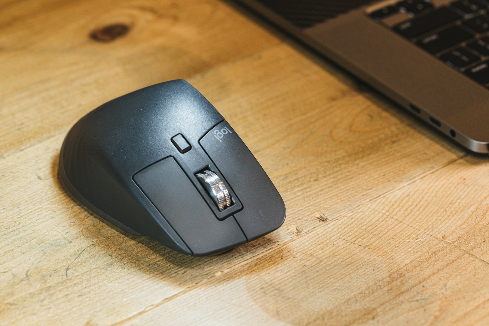 A gray wireless mouse placed on a wooden desk