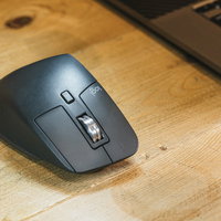 木製デスク上に置かれたグレーのワイヤレスマウスの写真