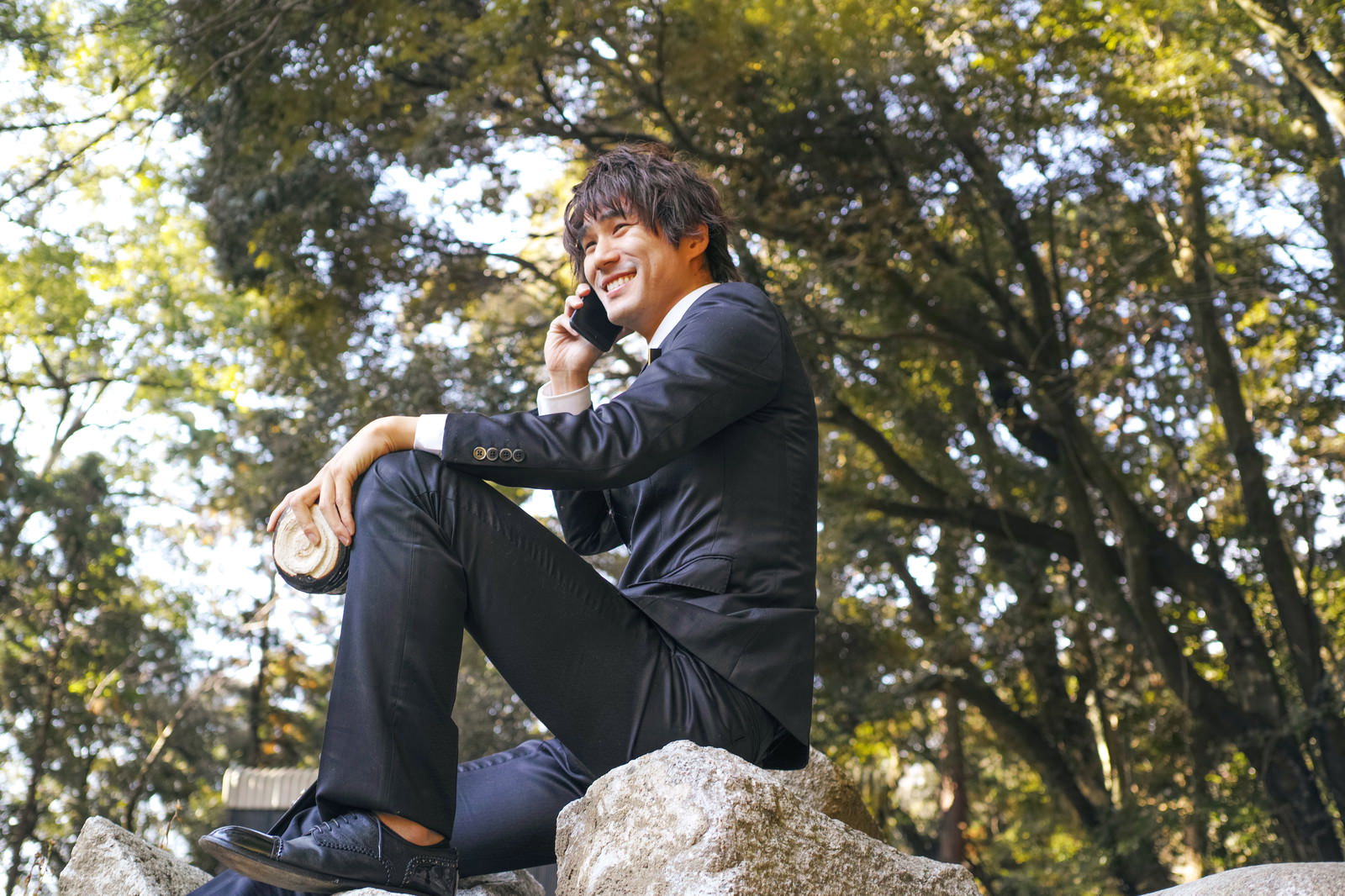 屋外で電話をかけながら笑顔を見せるスーツ姿のサラリーマン男性［モデル：村田裕章］