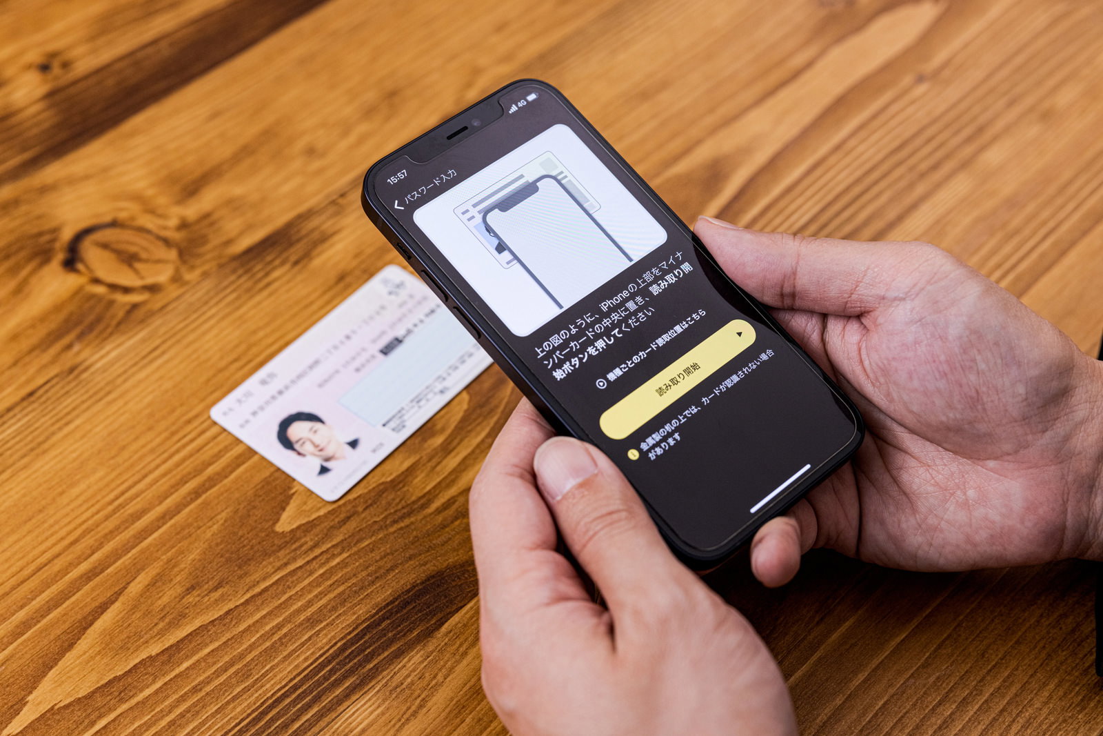 木製テーブルでマイナンバーカードをスマートフォンで読み取る手［モデル：大川竜弥］
