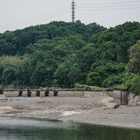 漏水の影響で水位が下がり湖底部分が見える中に建つ旧頭首工船通閘門跡と排砂門跡の写真