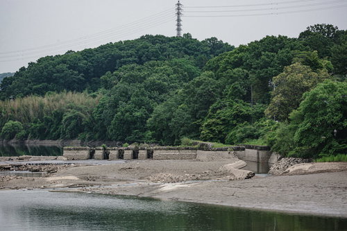 漏水の影響で水位が下がり湖底部分が見える中に建つ旧頭首工船通閘門跡と排砂門跡