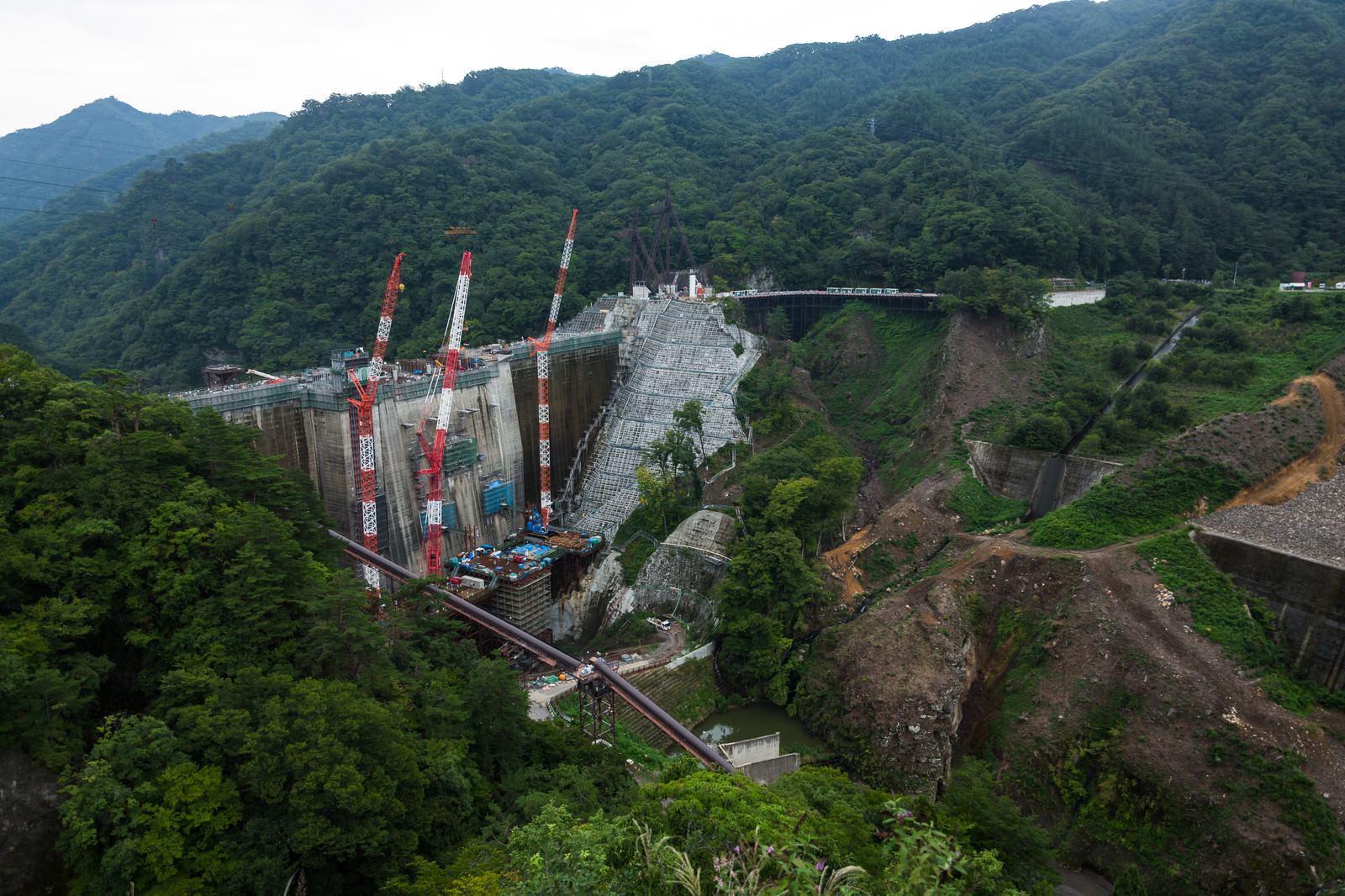 緑の山々に囲まれた谷間で建設工事が進む八ッ場ダムと複数のクレーン