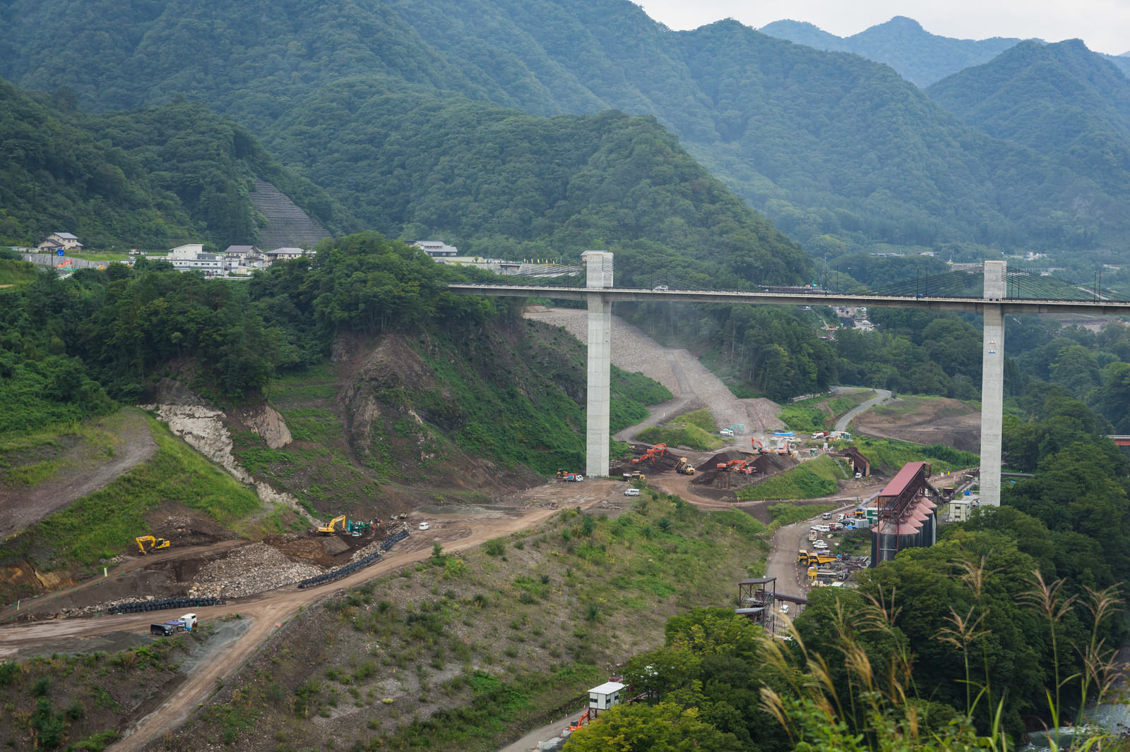 緑の山々に囲まれた渓谷に架かる白い橋とダム建設現場