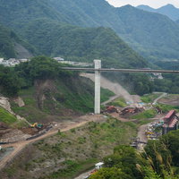 緑の渓谷で進む八ッ場ダム工事と新設橋梁の建設現場の写真