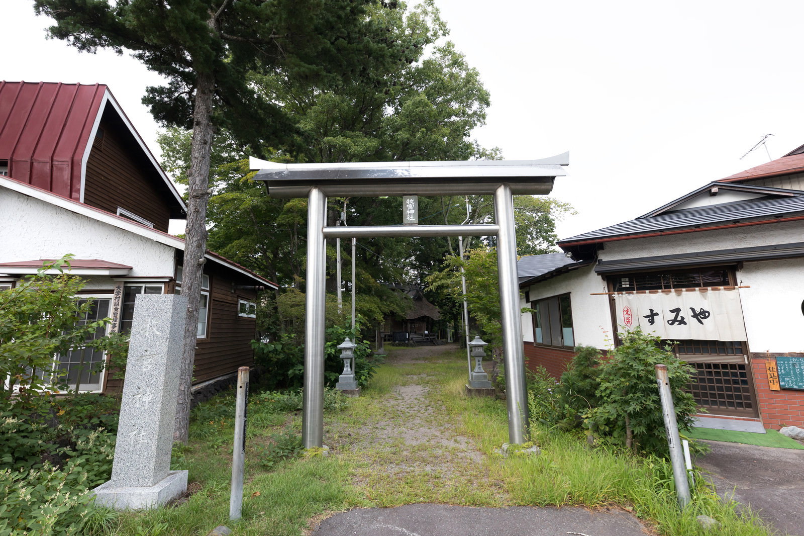 緑の木々に囲まれた参道に立つ牧宮神社の朱色の鳥居