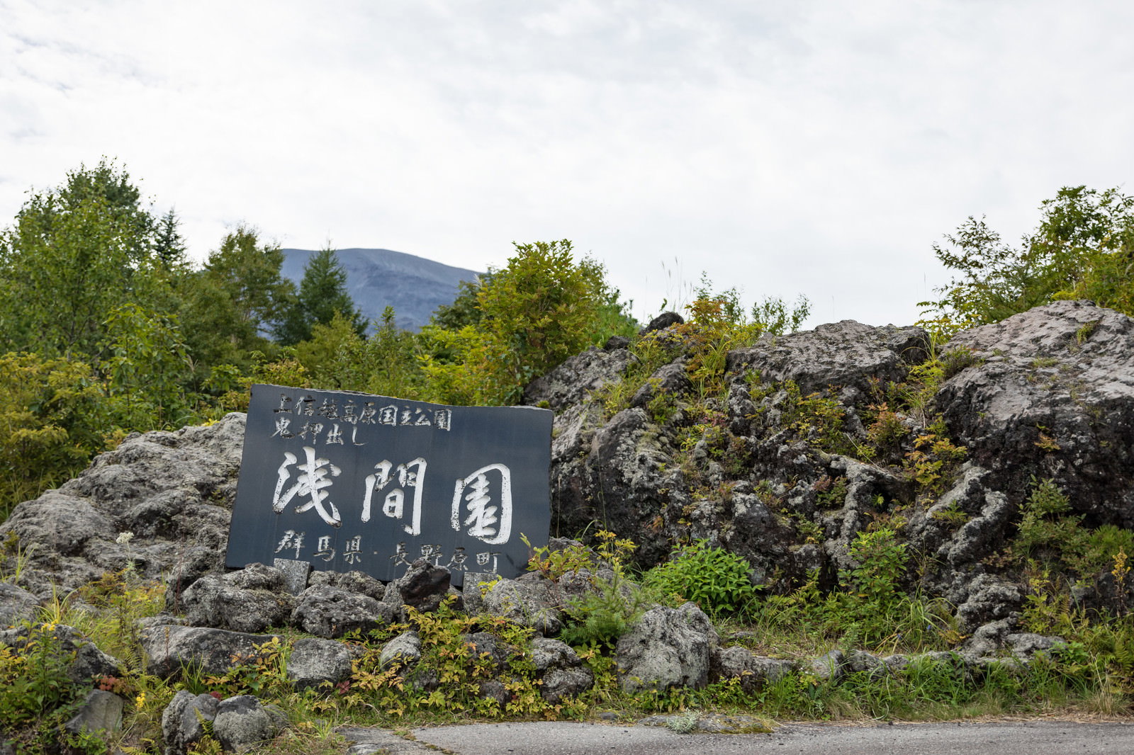 黒い石製看板に白文字で「浅間園」と刻まれ、背景に溶岩岩場と緑の樹木が広がる風景