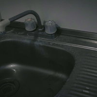 汚れた流し台と水栓、黒いプラスチック製シンクの劣化状態の写真