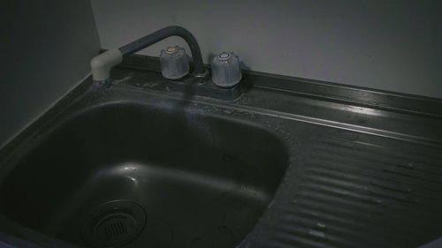 汚れた流し台と水栓、黒いプラスチック製シンクの劣化状態