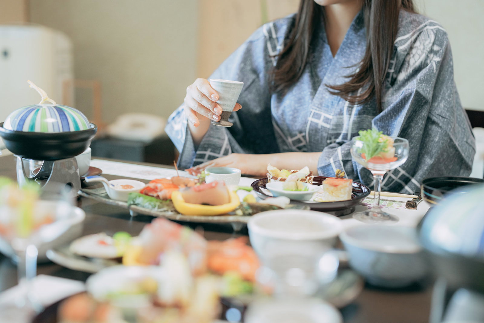 会席料理のテーブルで食事をする浴衣姿の女性［モデル：石投げて美奈代］
