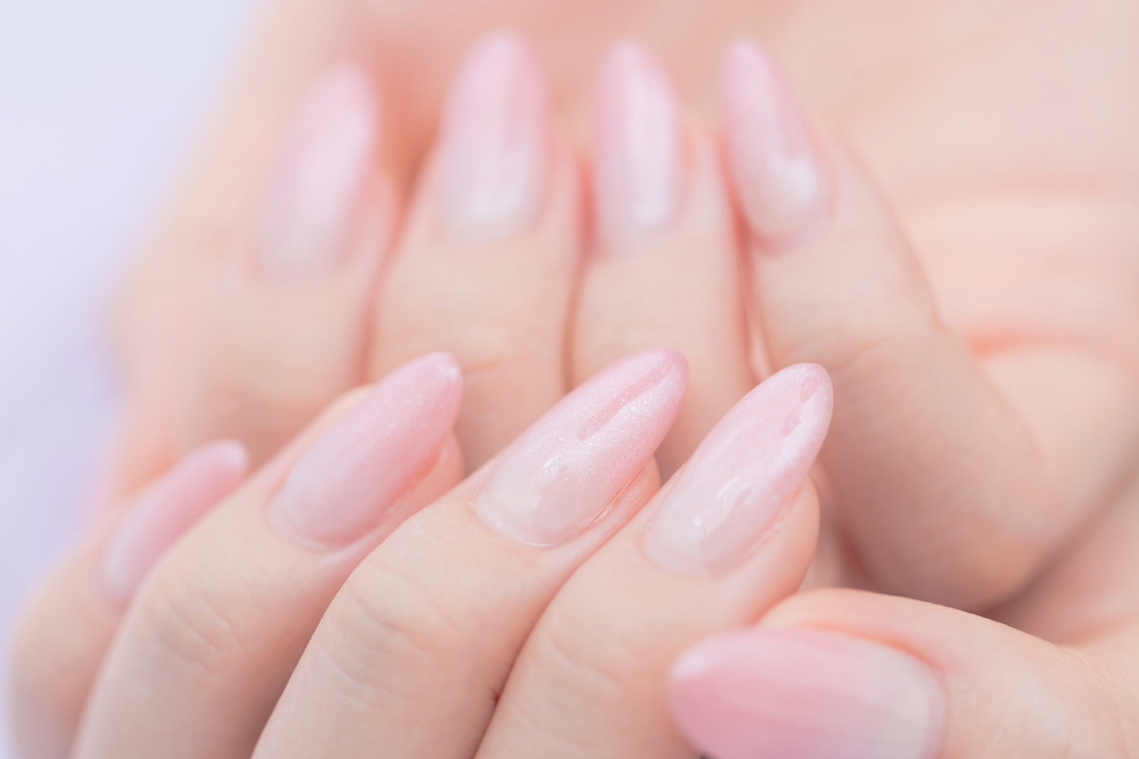 薄いピンクのネイルカラーを施した両手を重ねた美しい指先