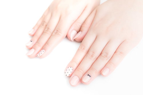 薄いピンクのベースに白いフラワーデザインのネイルをした爪