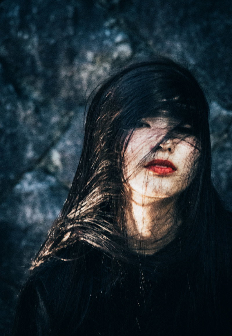 暗い背景で髪が乱れてボサボサになった女性が赤い口紅をつけている［モデル：なんこ］