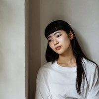 白い壁に寄りかかってぼんやりと遠く見つめる女性の写真