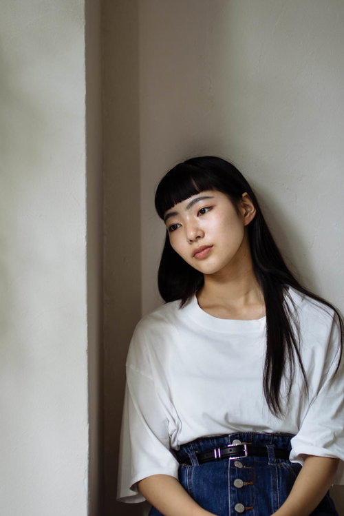 白い壁に寄りかかってぼんやりと遠く見つめる女性