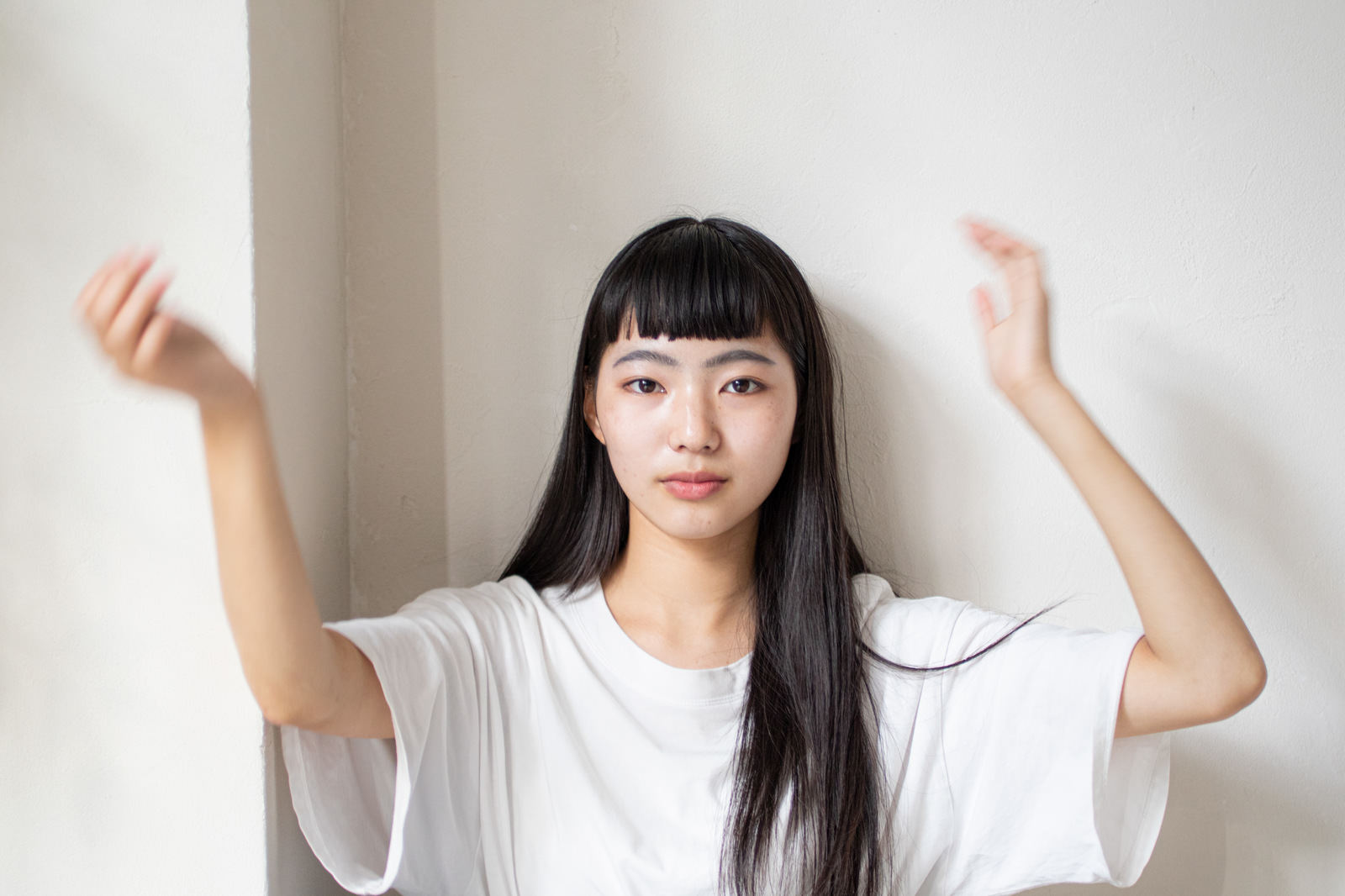 白いTシャツを着た女性が真顔で両手を上げて手振りをしている［モデル：なんこ］