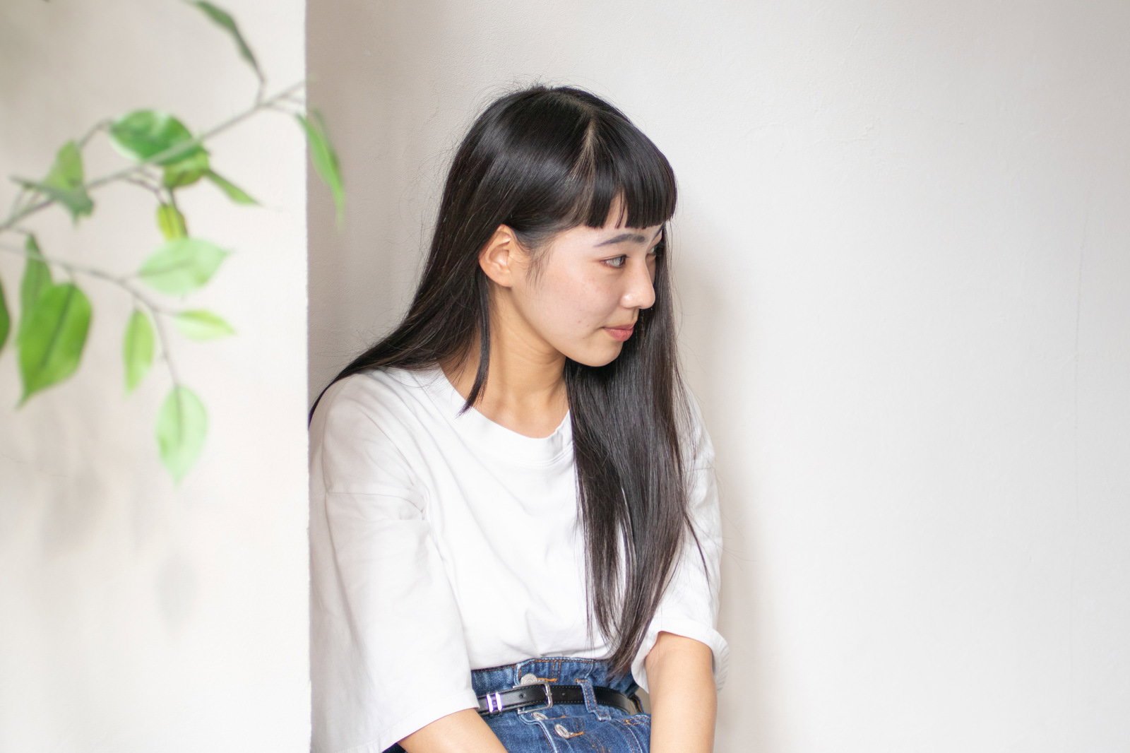 観葉植物の近くで控えめに座る白い服の女性［モデル：なんこ］