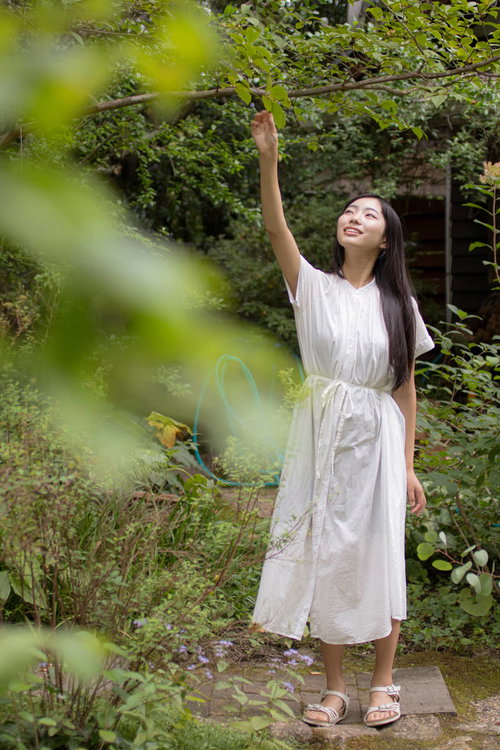 庭園で枝に手を伸ばす白いワンピースの女性