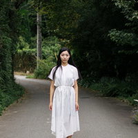 緑に囲まれた道で棒立ちするワンピース姿の女性の写真