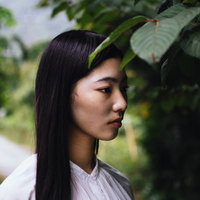木陰でぼんやりと前を見つめる女性のポートレートの写真
