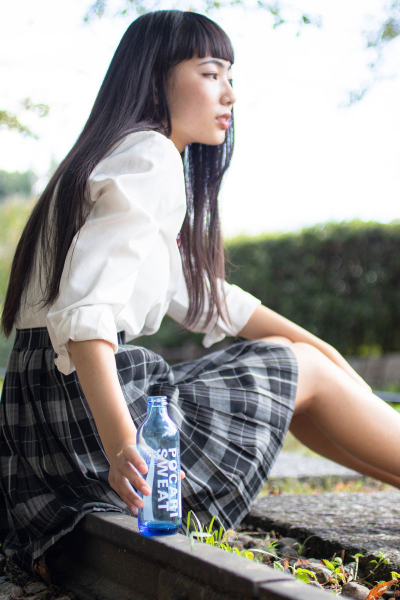 ベンチに座って飲み物を飲む制服姿の女子高生［モデル：なんこ］