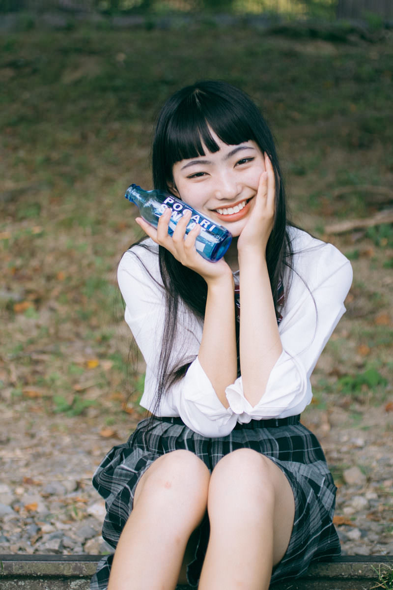 ベンチに座ってポカリを持ち微笑む制服姿の女子高生［モデル：なんこ］