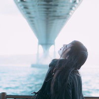 海と橋を背景に空を見上げる女性のポートレートの写真