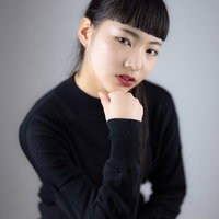 黒いニットを着て頬杖を突くオン眉ヘアスタイルの女性の写真