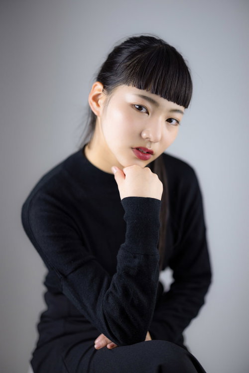 黒いニットを着て頬杖を突くオン眉ヘアスタイルの女性