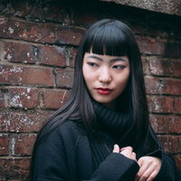 レンガ壁の前ですまし顔をするツンとした女性の写真