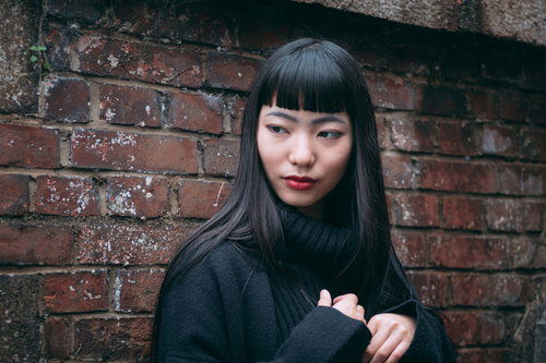 レンガ壁の前ですまし顔をするツンとした女性