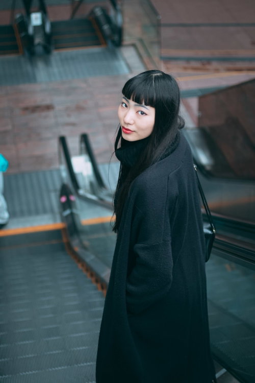エスカレーターで後ろを振り返る黒髪の女性