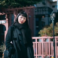 黒いコートとマフラーで待ち合わせする、オン眉の女性の写真