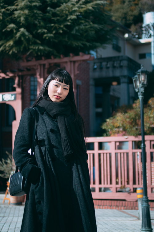 黒いコートとマフラーで待ち合わせする、オン眉の女性