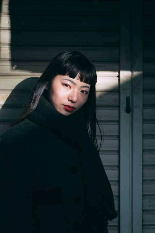 シャッター前で視線を向ける影と女性のオン眉ポートレート